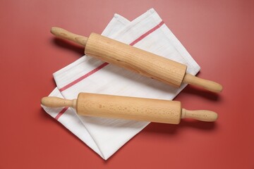 Wooden rolling pins and napkin on red background, flat lay