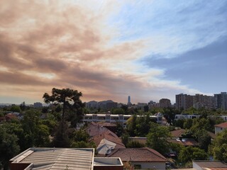 Santiago City under Smoky Sky and clouds. Araucaria tree, skyscraper, and San Cristobal hill at background.