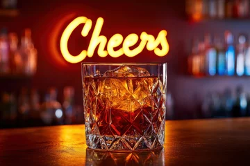 A whiskey old-fashioned in a crystal tumbler, bathed in warm amber light with a neon sign reading "Cheers" in the background