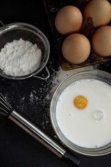 the process of preparing dough with egg, milk, flour and tools for kneading dough on a dark background, different angles