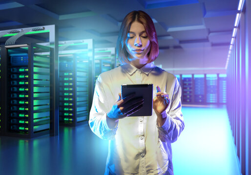 A data center with a network engineer managing server racks using a tablet, illuminated by blue and green LED lights in a high-tech environment.