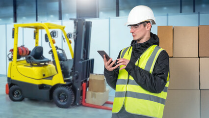 Man warehouse employee. Loader stands near forklift with boxes. Warehouse employee writes SMS to customer. Storekeeper with telephone. Man warehouse employee in yellow vest and helmet