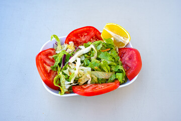Green salad with arugula, lamb and tomatoes. Healthy vegan dish. Top view at table. Turkish Coban (choban) salata or Shepherds salad, Akdeniz salad in white bowl.