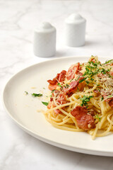 Close-up view of delicious plate of spaghetti carbonara with bacon and herbs on a white marble table