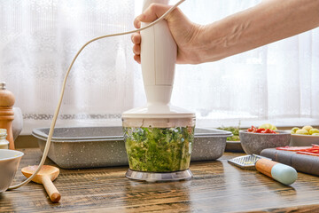 Preparing fresh green ingredients with an immersion blender in a cozy kitchen setting