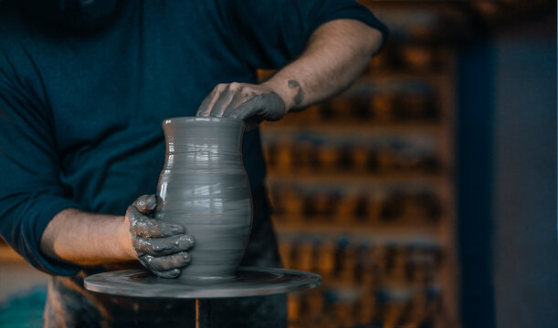 A skilled artisan molds clay on a pottery wheel, focusing intently on shaping a vase with hands covered in wet clay in a workshop setting.