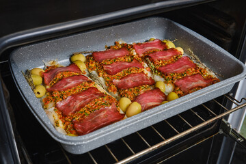 Delicious roasted fish topped with savory bacon and green olives in the oven