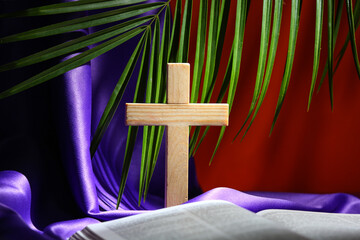 Wooden cross with purple cloth, palm leaf and Bible on red background. Good Friday concept