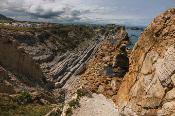 Dramatic coastal cliffs with layered rock formations overlooking the sea under a cloudy sky