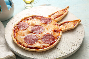 Wooden board with tasty pizza for Easter celebration on blue background