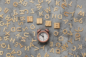 Text TIME, alarm clock and wooden letters on grey grunge background. Top view