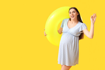 Young pregnant woman with inflatable ring on yellow background. Travel concept