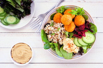 Healthy homemade salad bowl with falafels, hummus, quinoa and vegetables. Overhead view table scene on a white wood background.