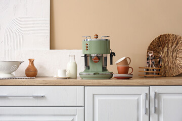 Modern coffee machine with cups and bottle of milk on table in kitchen
