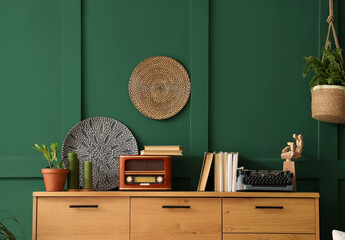 Vintage typewriter with books and radio receiver on commode near green wall in room