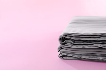 Stacked clean bed linens on pink background, closeup. Space for text
