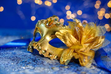 Beautiful carnival mask on blue glitter background against blurred lights, closeup. Bokeh effect