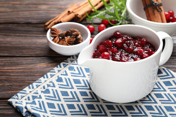 Tasty cranberry sauce in gravy boat and spices on wooden table, closeup