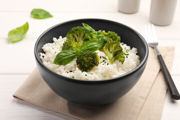 Tasty rice with broccoli and basil on white wooden table, closeup