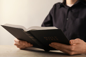 Woman reading Holy Bible at beige table, closeup