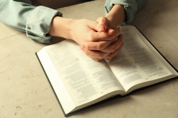 Woman with open Holy Bible in English language praying at beige table, closeup