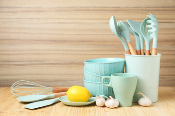 Dishware, cooking utensils, lemon and garlic on wooden table. Space for text