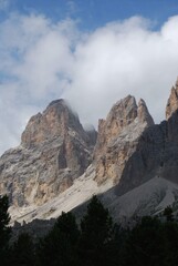 Majestic rocky mountain peaks rise against a blue sky, with pine trees at the base, showcasing rugged natural beauty.