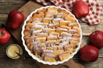 Delicious bread pudding with raisins, powdered sugar, condensed milk and apples on wooden table,...