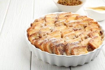 Delicious bread pudding with raisins and powdered sugar on white wooden table, closeup. Space for text