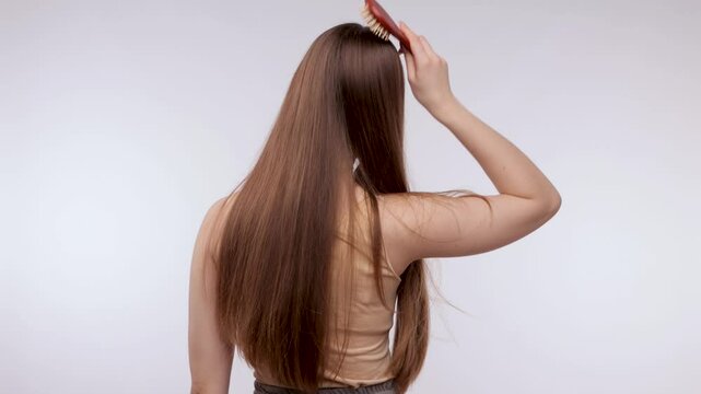 Young beautiful girl in a beige sweater with long hair. The girl combs her hair with a comb