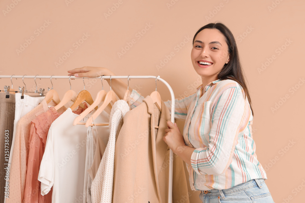 Wall mural Young woman near rack with clothes on beige background