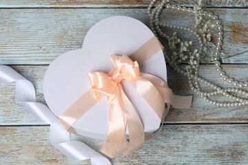 Beautiful wedding gift, pearl jewelry, ribbon and gypsophila flowers on wooden table, flat lay