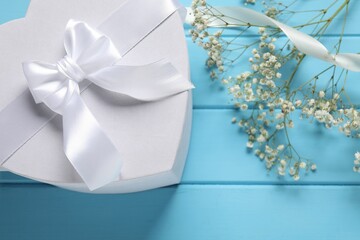 Beautiful wedding gift, ribbon and gypsophila flowers on light blue wooden table, flat lay