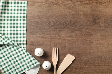Checkered tablecloth, cooking utensils and spices on wooden table, flat lay. Space for text