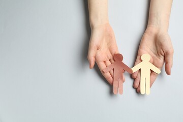 Stop racism. Woman holding human paper figures of different colors on light grey background, top...