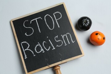 Chalkboard with phrase Stop Racism and tangerines of different colors on light grey background, top...