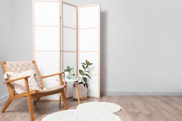 Fototapeta premium Interior of light room with folding screen, armchair and table