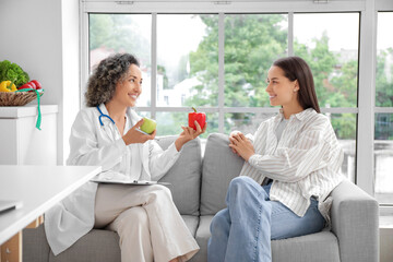 Mature female nutritionist showing healthy food to client on sofa in kitchen