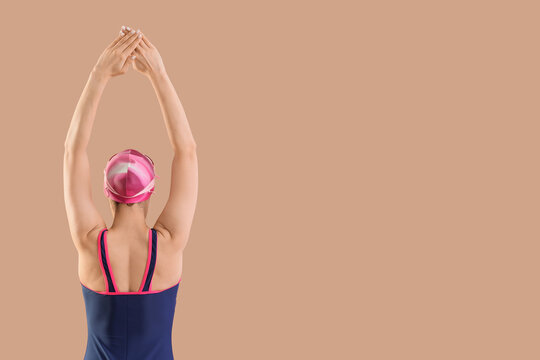 Professional young female swimmer stretching on beige background, back view