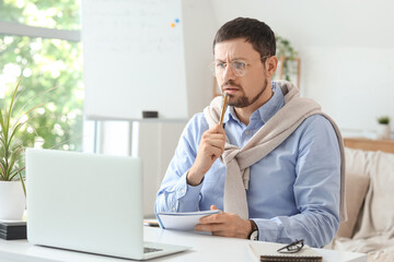 Naklejka premium Confused young male teacher with laptop and notebook giving online lesson at home