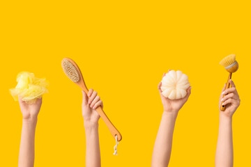 Female hands with massage brushes and bath sponges on yellow background