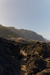 Obraz premium Man-made concrete footpath through volcanic rocky beach in Garachico, Tenerife. Vertical view towards the afternoon sun and coastal mountains.