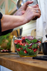 A woman stirring vegetable salad in a glass bowl, side view
