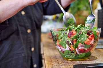 A woman stirring vegetable salad in a glass bowl, side view