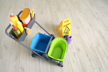 Trolley with cleaning supplies and caution sign on wooden floor at home