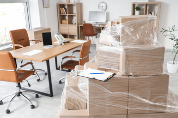 Wrapped cardboard boxes with stretch film and clipboard in office on moving day