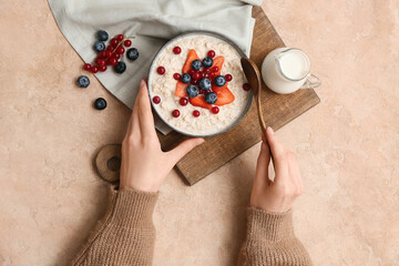 Female hands with tasty oatmeal and different berries in bowl on beige grunge background