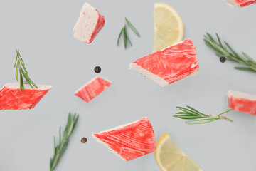 Cut tasty crab stick with rosemary, peppercorns and slices of lemon flying on grey background © Pixel-Shot