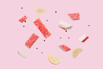 Cut tasty crab sticks with peppercorns and slices of lemon flying on pink background © Pixel-Shot