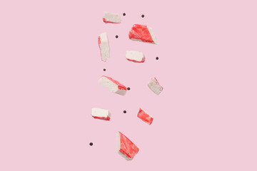 Cut tasty crab stick and peppercorns flying on pink background